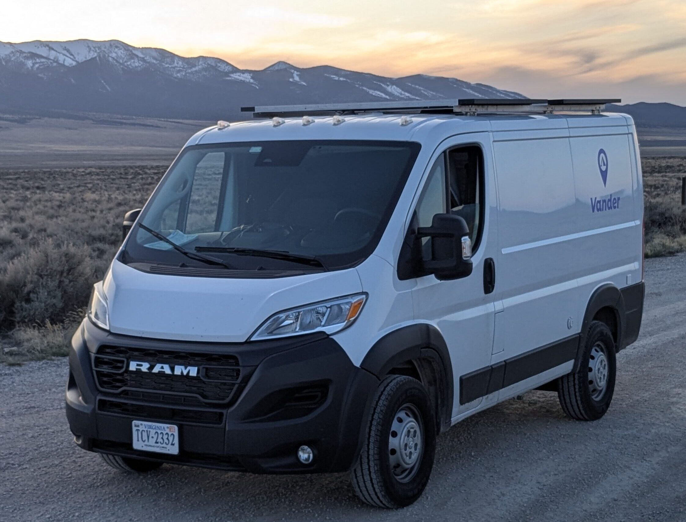 Medium white campervan on the side of the road in the high desert getting ready to camp for the night with the sun setting over the mountains in the background.