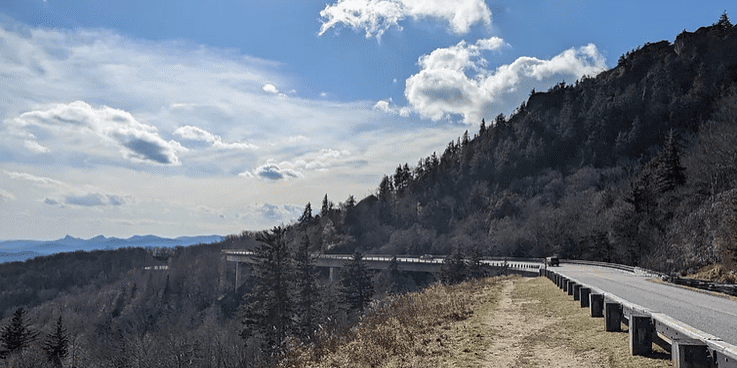 Partner camper road trip picture of blue ridge parkway winding through the mountains outdoors under a blue sky.