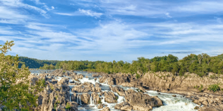 View of river rapids through a rocky channel under a blue sky and wispy clouds